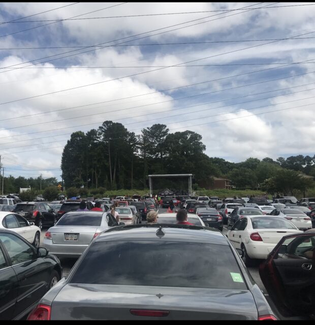 Drive-in event with outdoor stage and LED wall, viewed from packed parking lot”